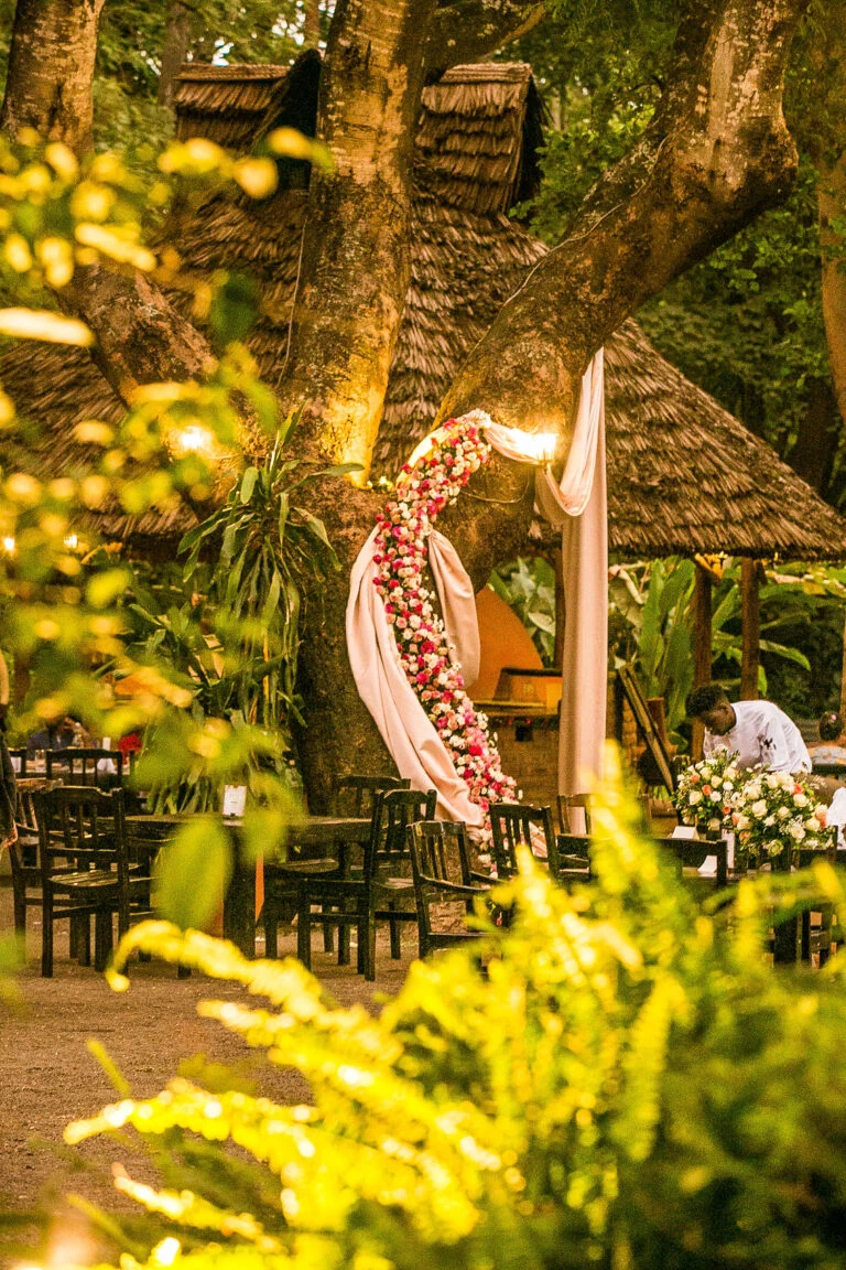 Tree trunk draped with fabric and a red and white flower garland above garden tables