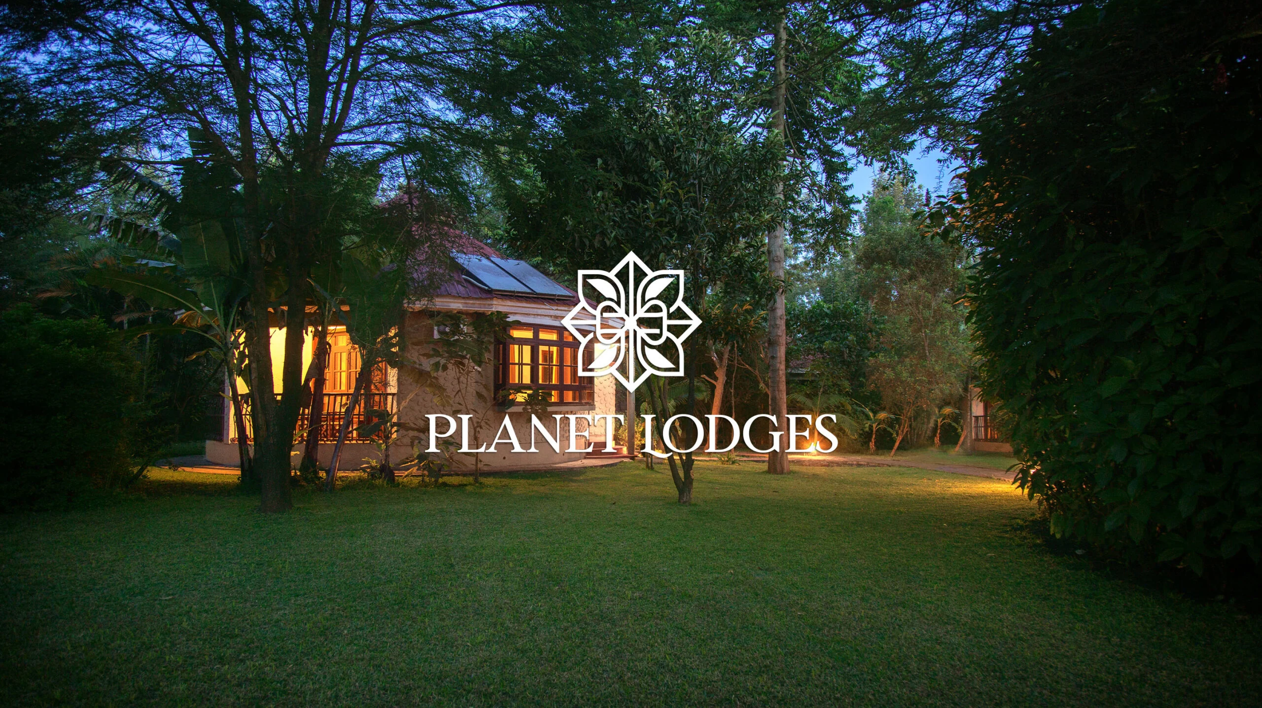 Planet Lodges logo in white over a lamp-lit cottage among trees at dusk