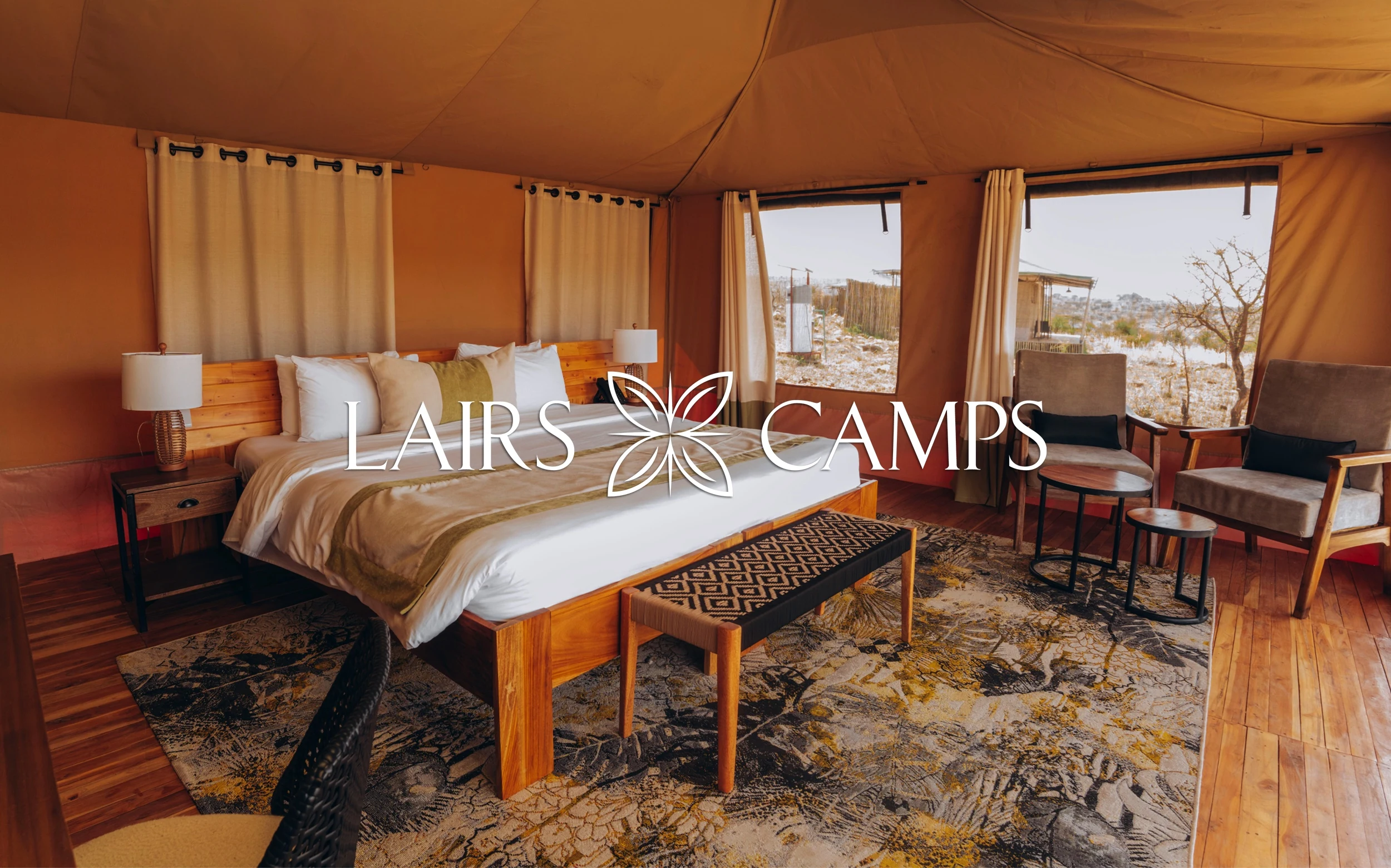 A Lairs Camps tent with the bed made up, and the Lairs Camps logo